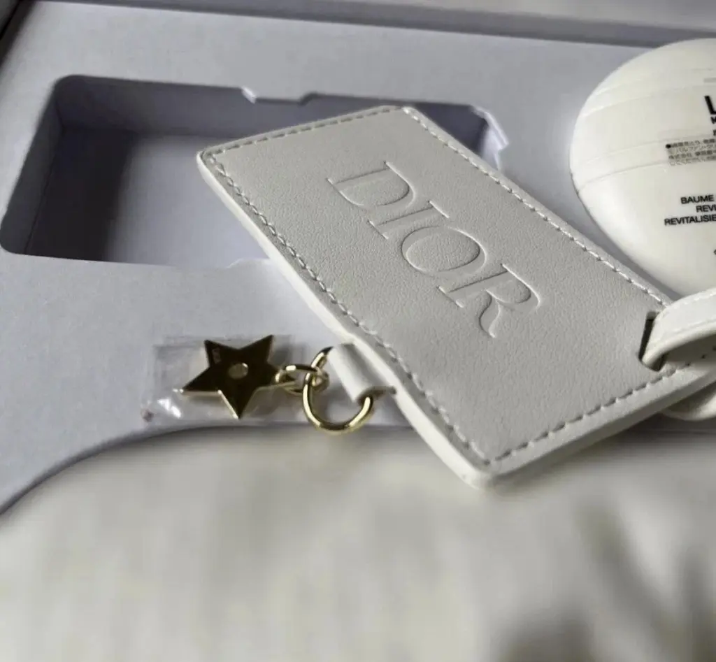 مجموعة هدايا عيد الميلاد للأعضاء من الفئة البلاتينية لعام 2026: كريم Dior Le Baume (سعة 50 مل)، وقناع للعينين، وبطاقة تعريف للأمتعة.